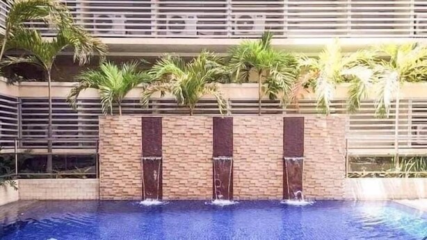 A swimming pool with a waterfall feature, surrounded by palm trees and a brick wall. - 150 Newport condotel pasay  (Pasay)