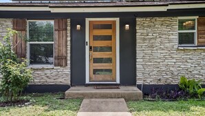 Une maison moderne avec une façade en pierre, une porte d’entrée en bois et un petit jardin devant la maison, agrémenté de plantes.