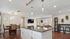 A modern kitchen with a central island, dining area, and a flat-screen TV mounted on the wall.