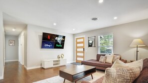 A modern living room with a flat-screen TV mounted on the wall, a brown leather sofa, a wooden coffee table, and a white console table.
