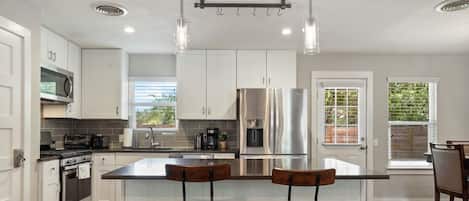 A modern kitchen with white cabinets, stainless steel appliances, and a central island with bar stools.