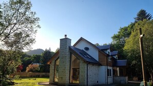 A modern house with a stone chimney, large windows, and a well-maintained lawn. - Exceptional New Beautiful House in Trossachs Loch Lomond National P. Brig O Turk (Callander)