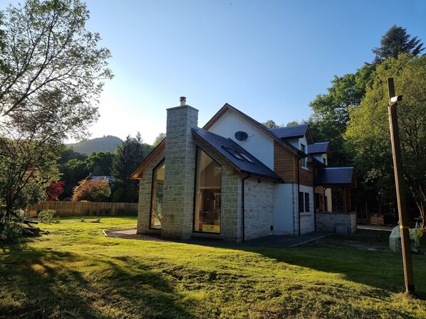 Ein modernes Haus mit einem Steinkamin, großen Fenstern und einem gepflegten Rasen.