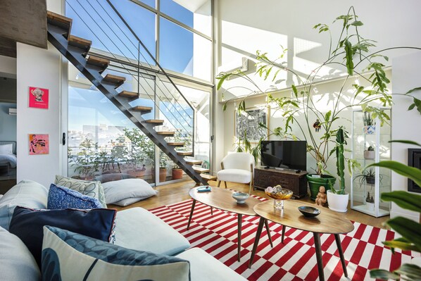 Un salon moderne avec un escalier, un téléviseur et diverses plantes.