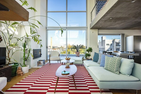 A modern living room with a large window, a sofa, a coffee table, and various plants.