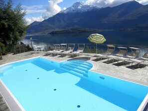 Una piscina con sillas de descanso y una sombrilla, rodeada de montañas y un lago.