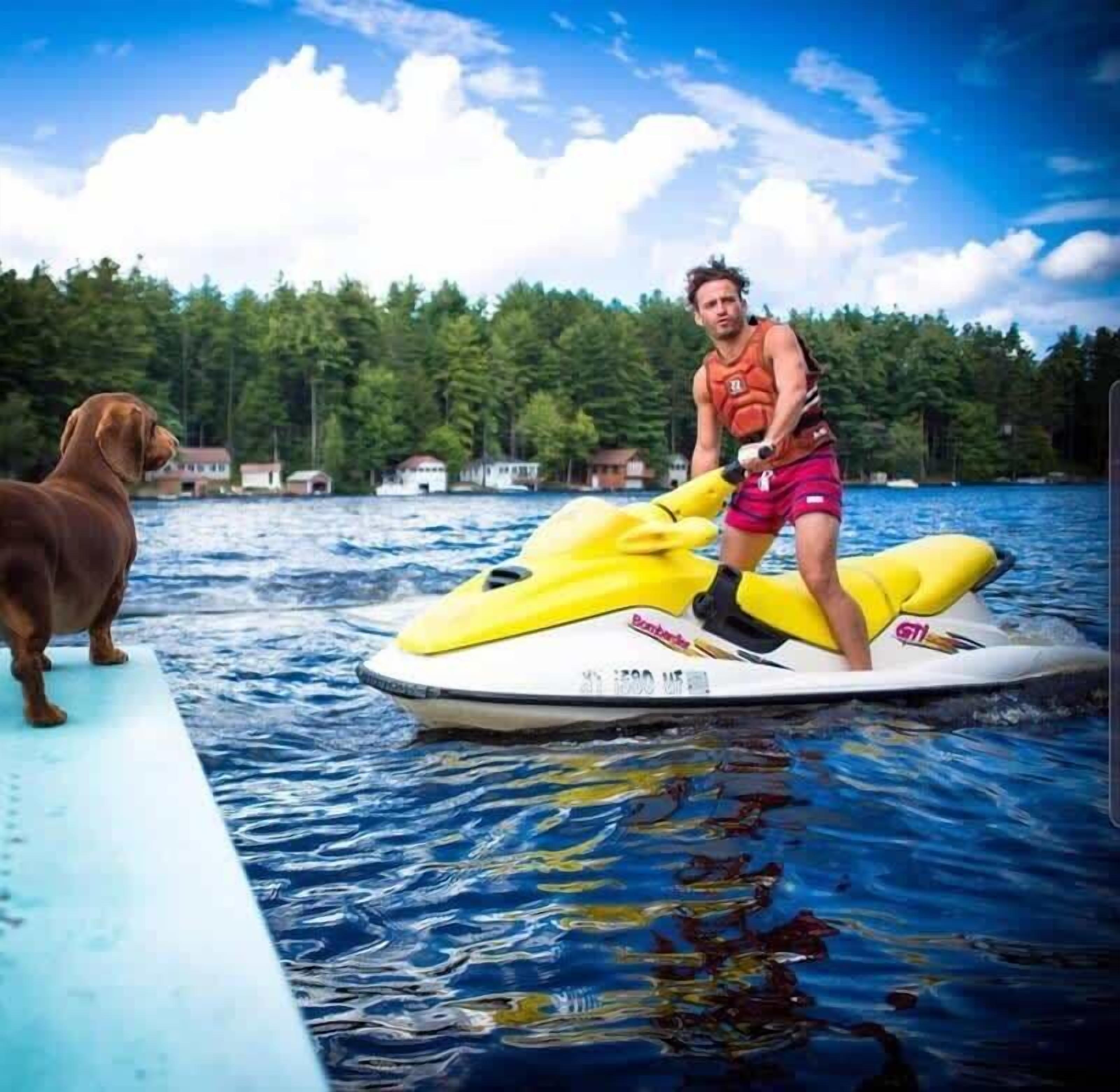 Una persona en un jet ski amarillo con un perro en un muelle.