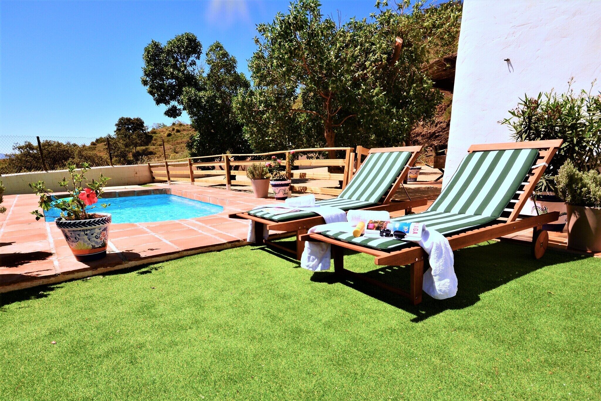 A poolside area with a rectangular pool, two lounge chairs, and potted plants.