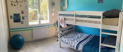 A room with a bunk bed, a large exercise ball, a window with a view of greenery, and a wall with a beach sign.