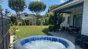 Un jardin avec un jacuzzi, une terrasse avec des chaises et un espace clos avec des arbres.