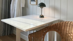 Ein Zimmer mit weißem Tisch, Korbstuhl und einer hängenden Pflanze.