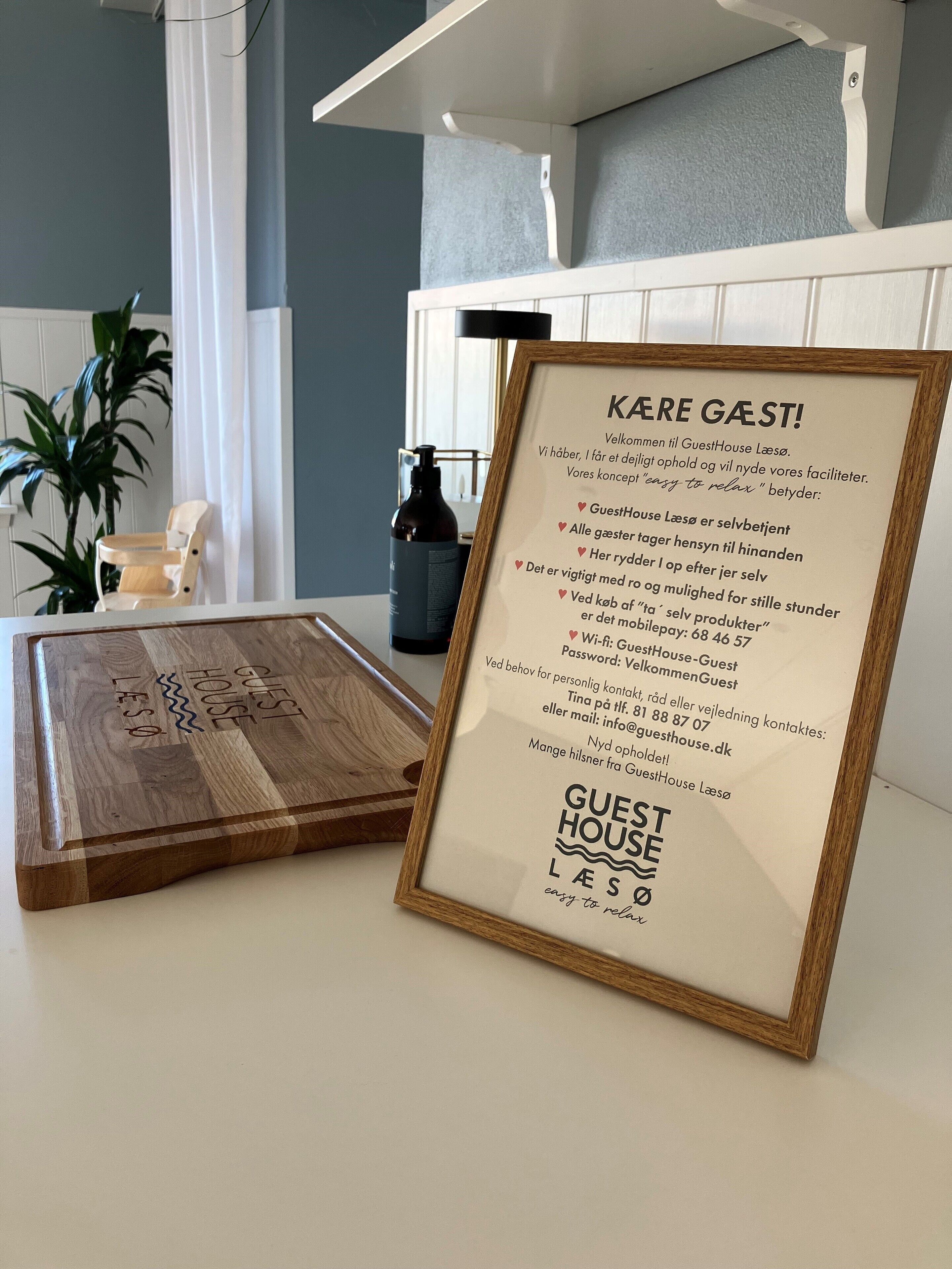 A framed welcome sign for GuestHouse Laeso, featuring amenities like Wi-Fi, a self-service kitchen, and a relaxing concept.