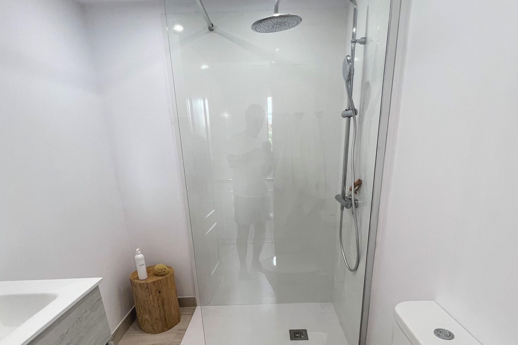 A modern bathroom with a glass-enclosed shower, a wooden stool with toiletries, and a white sink.