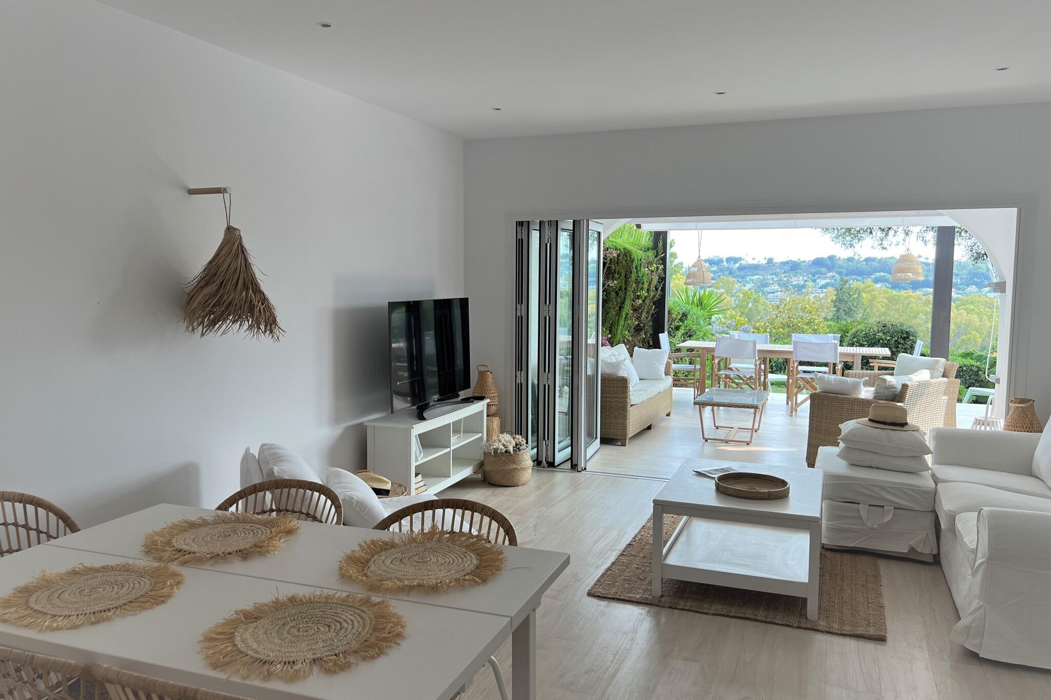 Amplia sala de estar con un televisor grande, muebles blancos y vistas al exterior.