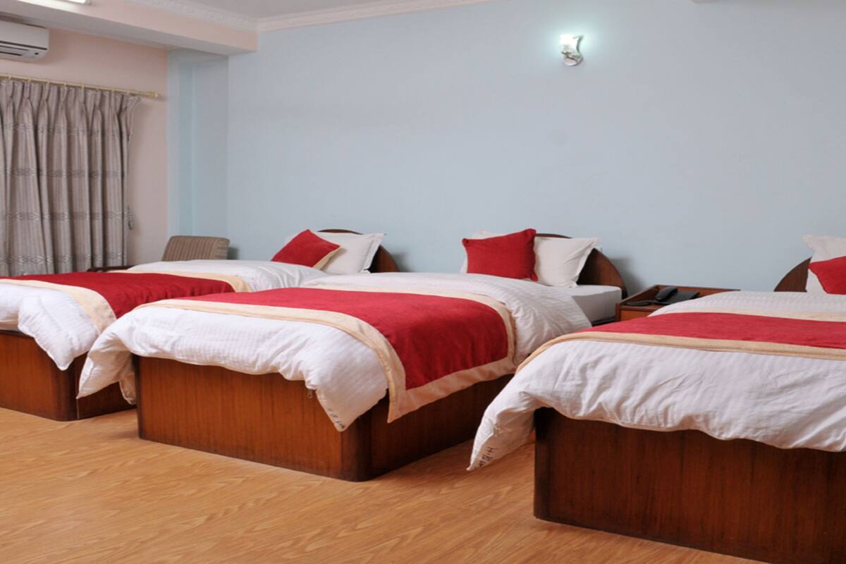 Een hotelkamer met drie houten bedden, elk voorzien van witte beddengoed en rode accenten.