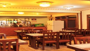 A restaurant with wooden tables and chairs, a bar area with bottles, and a refrigerator. - MeroStay 035 Hotel Brihaspati (Kathmandu)