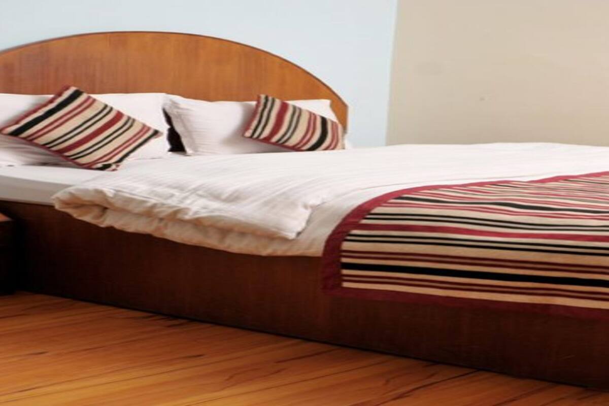 Een net opgemaakt bed met een houten hoofdbord, wit beddengoed en gestreepte kussens.
