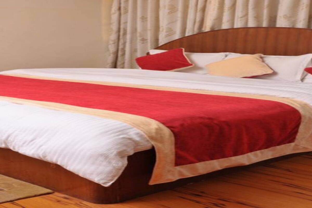 Een bed met een rood-witte dekbedovertrek, een houten hoofdbord en een beige gordijn op de achtergrond.