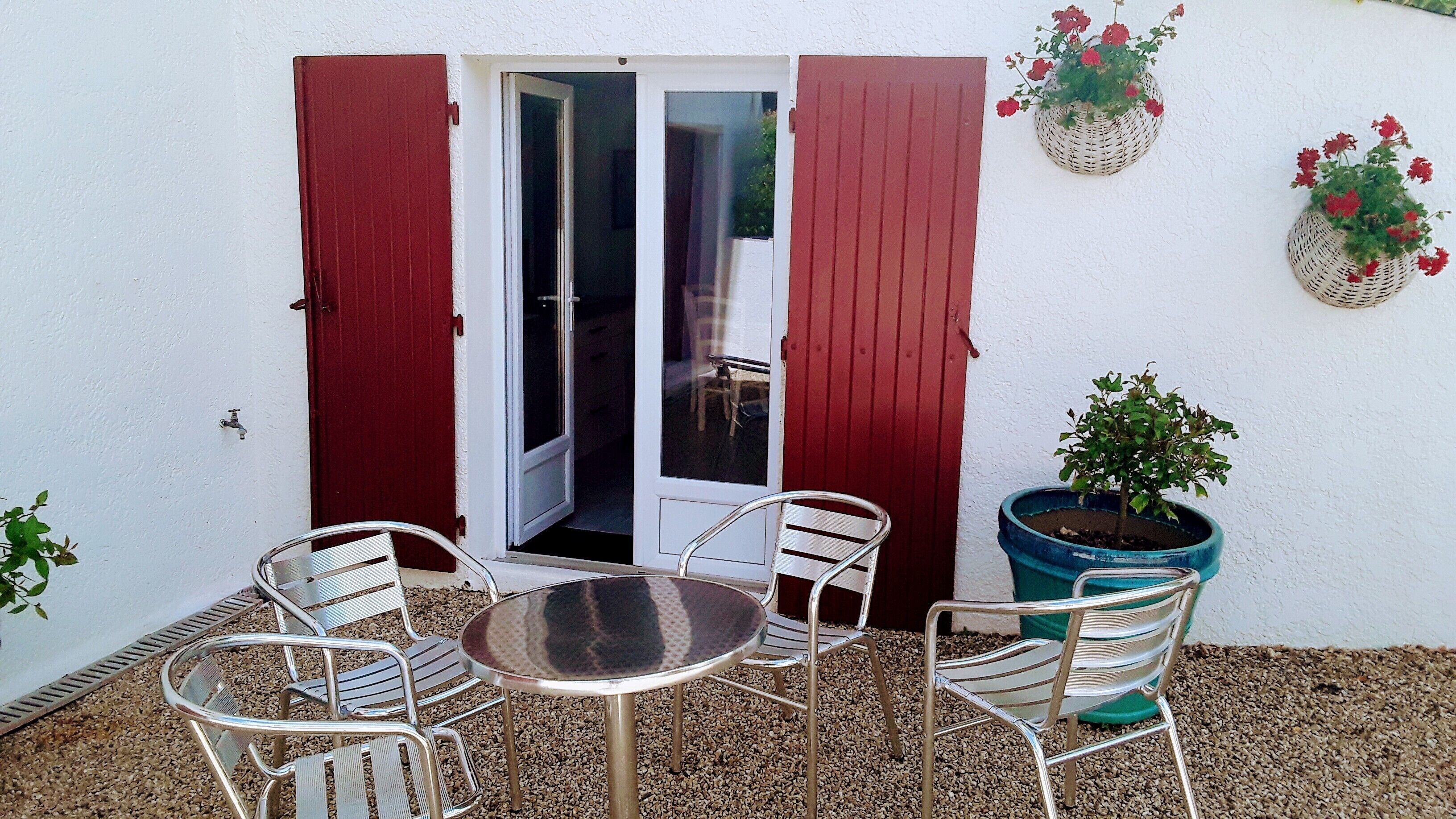A patio with a table and chairs, a potted plant, and a door with red shutters.