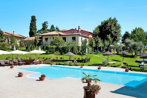 A swimming pool with lounge chairs and umbrellas, surrounded by greenery and a building with a red roof. - Apartment in Vinci with Pool & Wellness (Pinete Fucecchio)