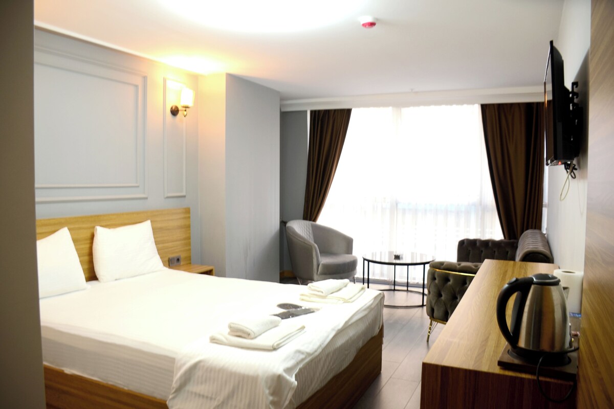 Ein Hotelzimmer mit einem Bett, einem Schreibtisch mit Wasserkocher, einem Sessel und einem an der Wand befestigten Fernseher.
