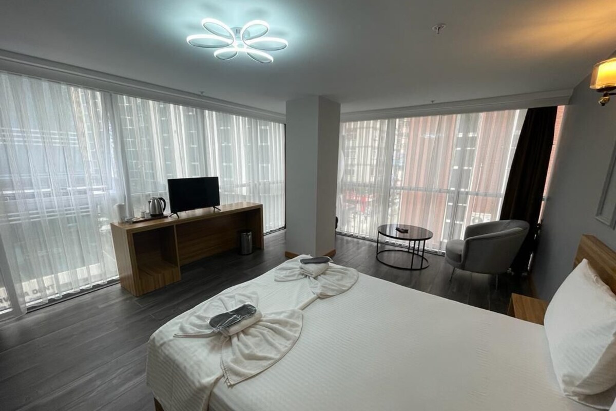 Ein Hotelzimmer mit einem großen Bett, einem Schreibtisch mit Fernseher, einem Sessel und Blick durch große Fenster.