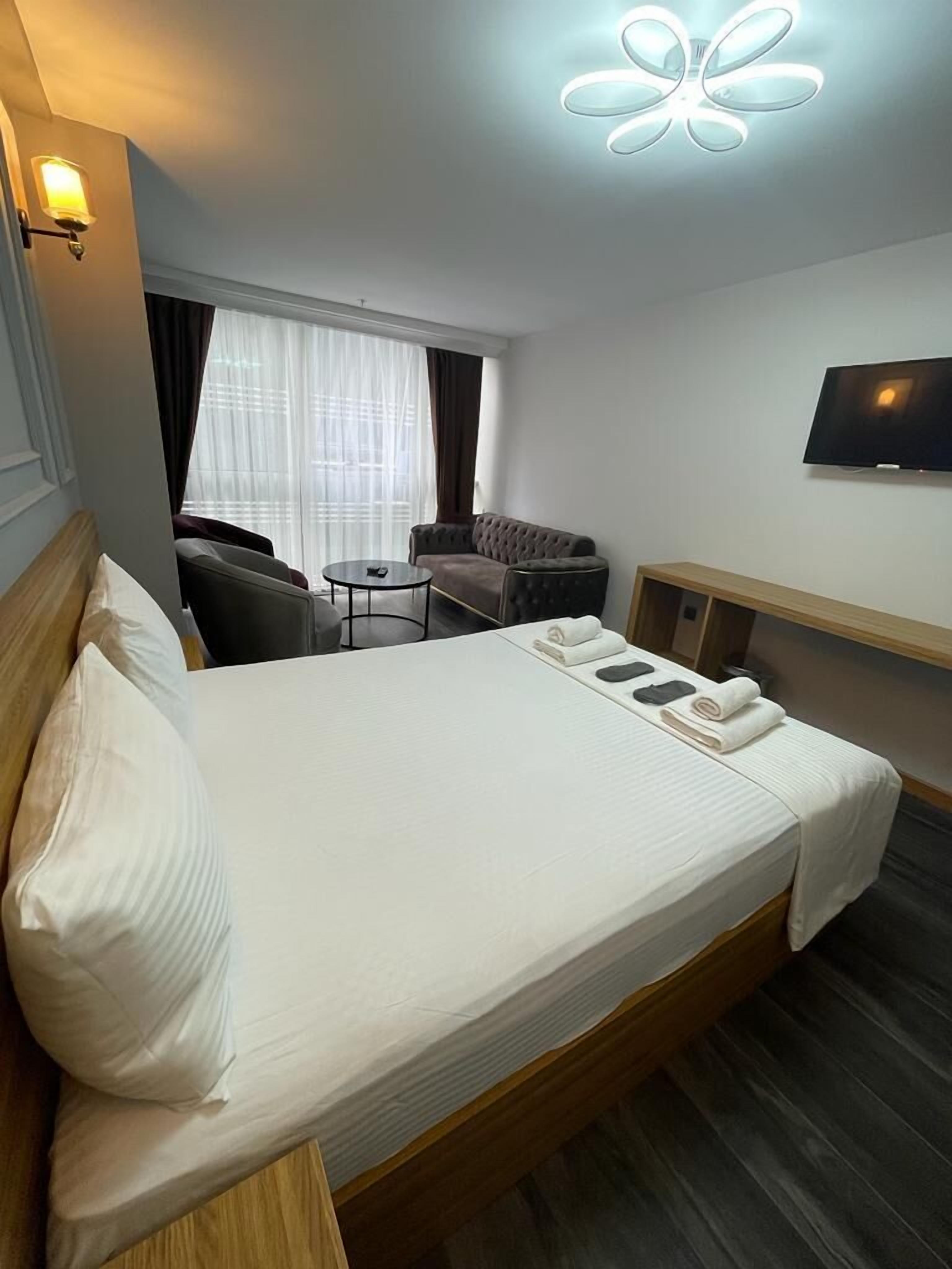 A hotel room with a large bed, a small round table, a sofa, a TV, and a window with curtains.