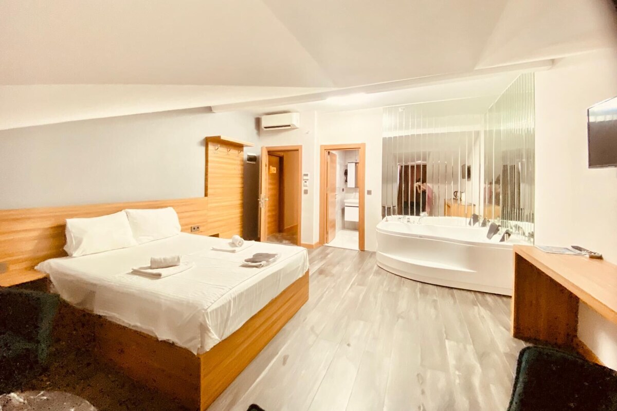 Ein modernes Hotelzimmer mit einem großen Bett, einem separaten Badezimmer mit Badewanne und einem Spiegel.