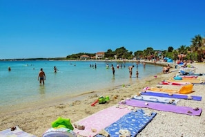 Una playa con gente nadando y tomando el sol, toallas coloridas y sillas de playa.