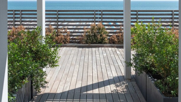 A wooden deck with a view of the ocean, white railings, and potted plants. - Kiss Beachfront Hotel & Restaurant (Cervia)