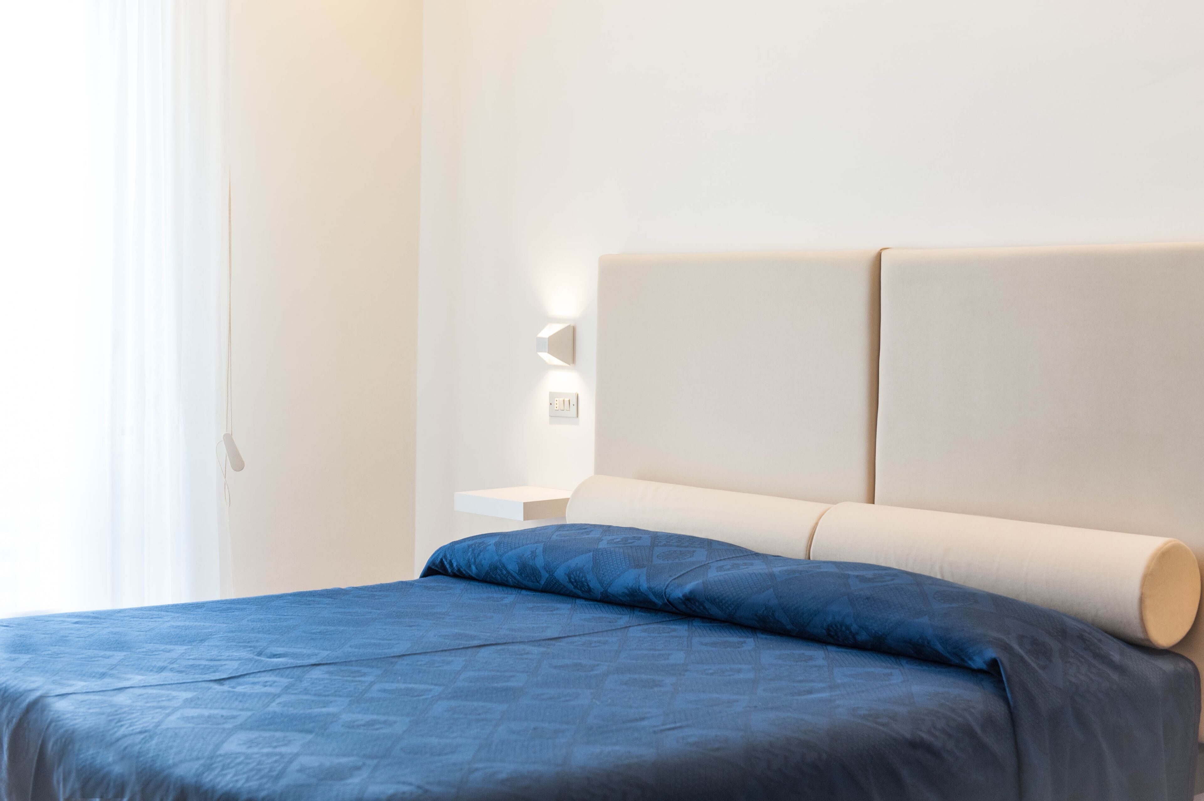 A neatly made bed with a blue bedspread and a cream-colored headboard.