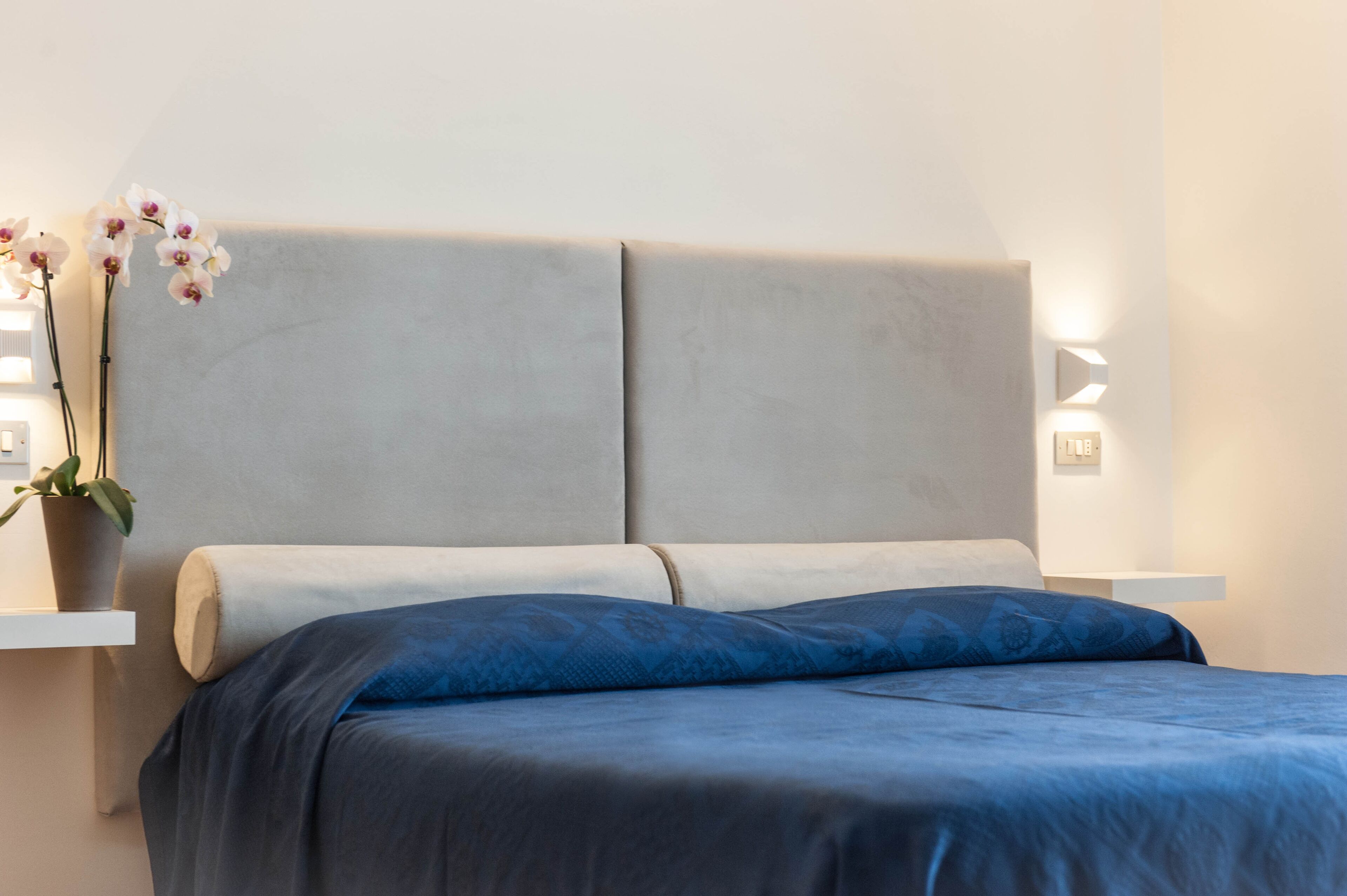 Un dormitorio con una cama grande, dos mesitas de noche y una lámpara fijada a la pared.