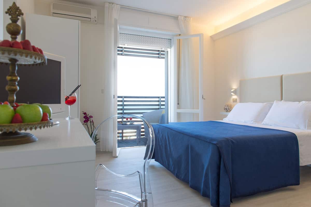 Habitación de hotel con cama, escritorio con fruta y bebida, una silla y vistas al exterior.