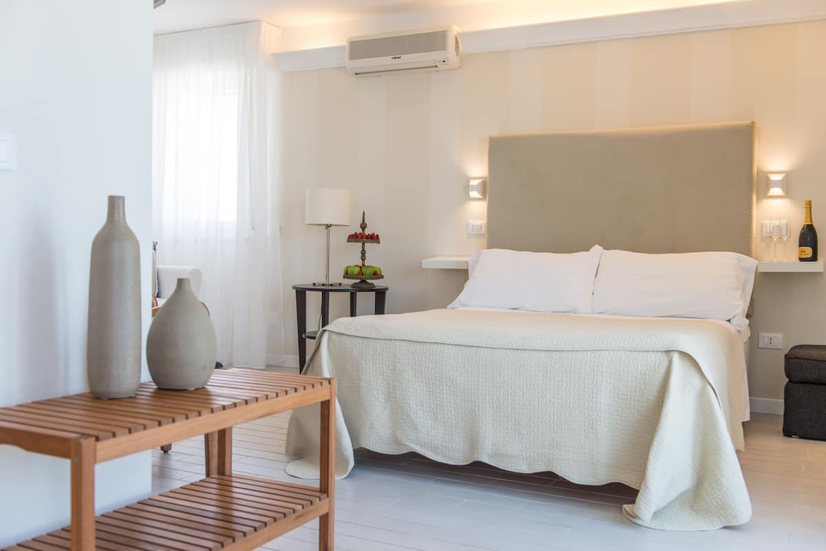 Una habitación de hotel con cama, mesitas de noche, lámpara y un florero.