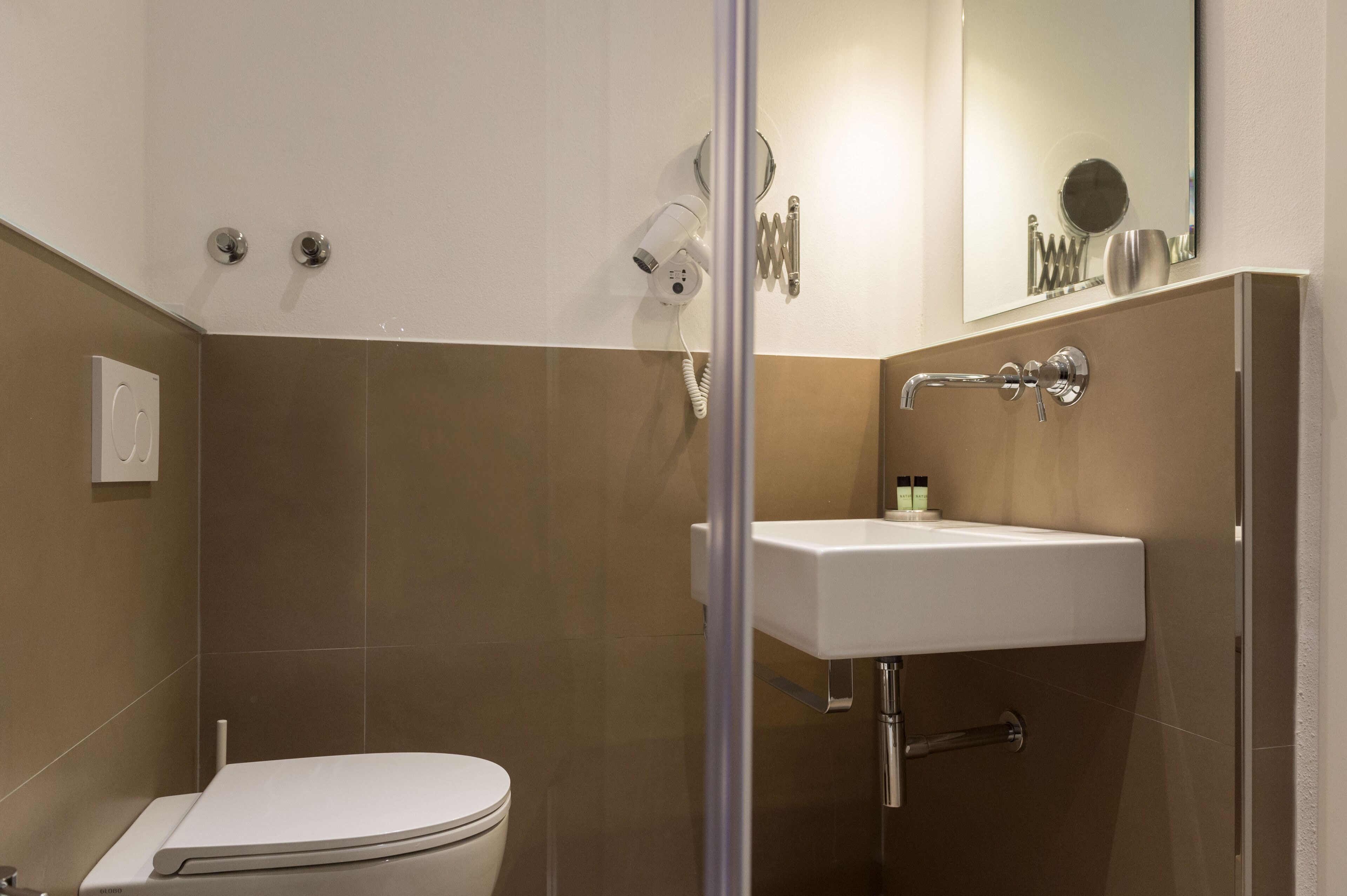 A bathroom with a toilet, a sink, a shower, and a mirror.