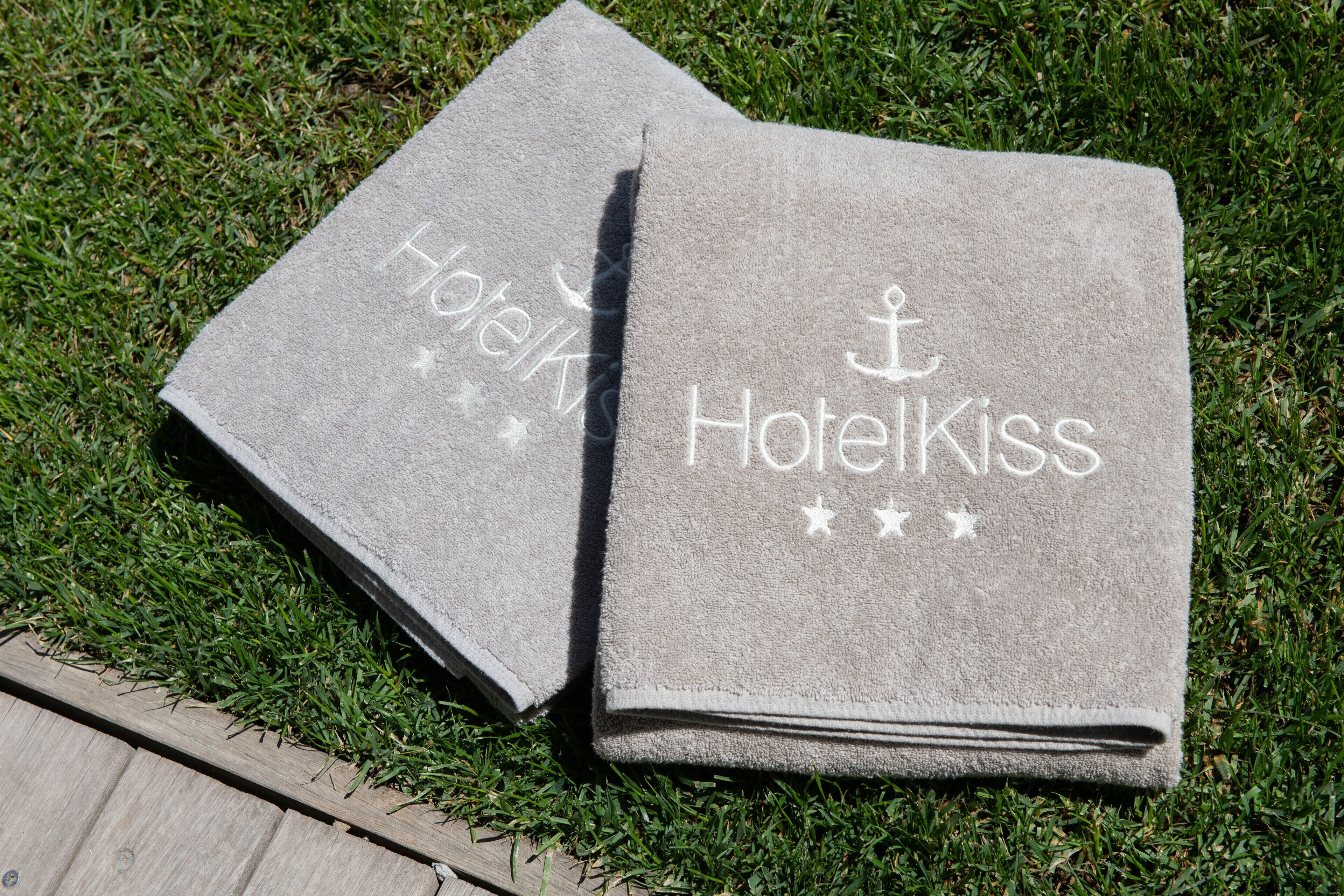 Duas toalhas dobradas com o texto "HotelKiss" e um símbolo de estrela.