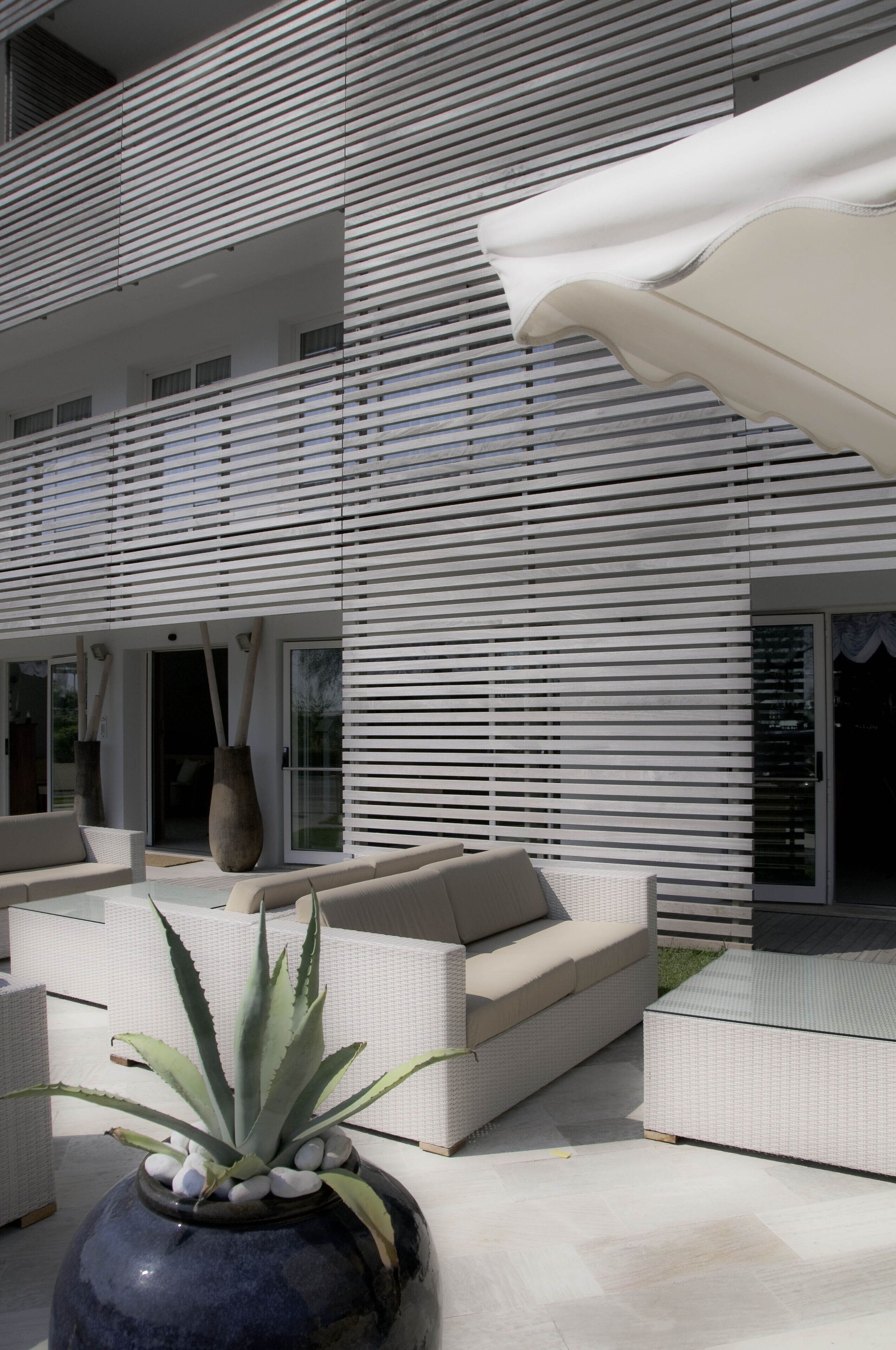 A modern outdoor seating area with white sofas and a large planter with an aloe plant.