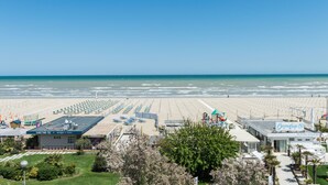 A beachside hotel with a large parking area, beach umbrellas, and a clear view of the ocean. - Kiss Beachfront Hotel & Restaurant (Cervia)