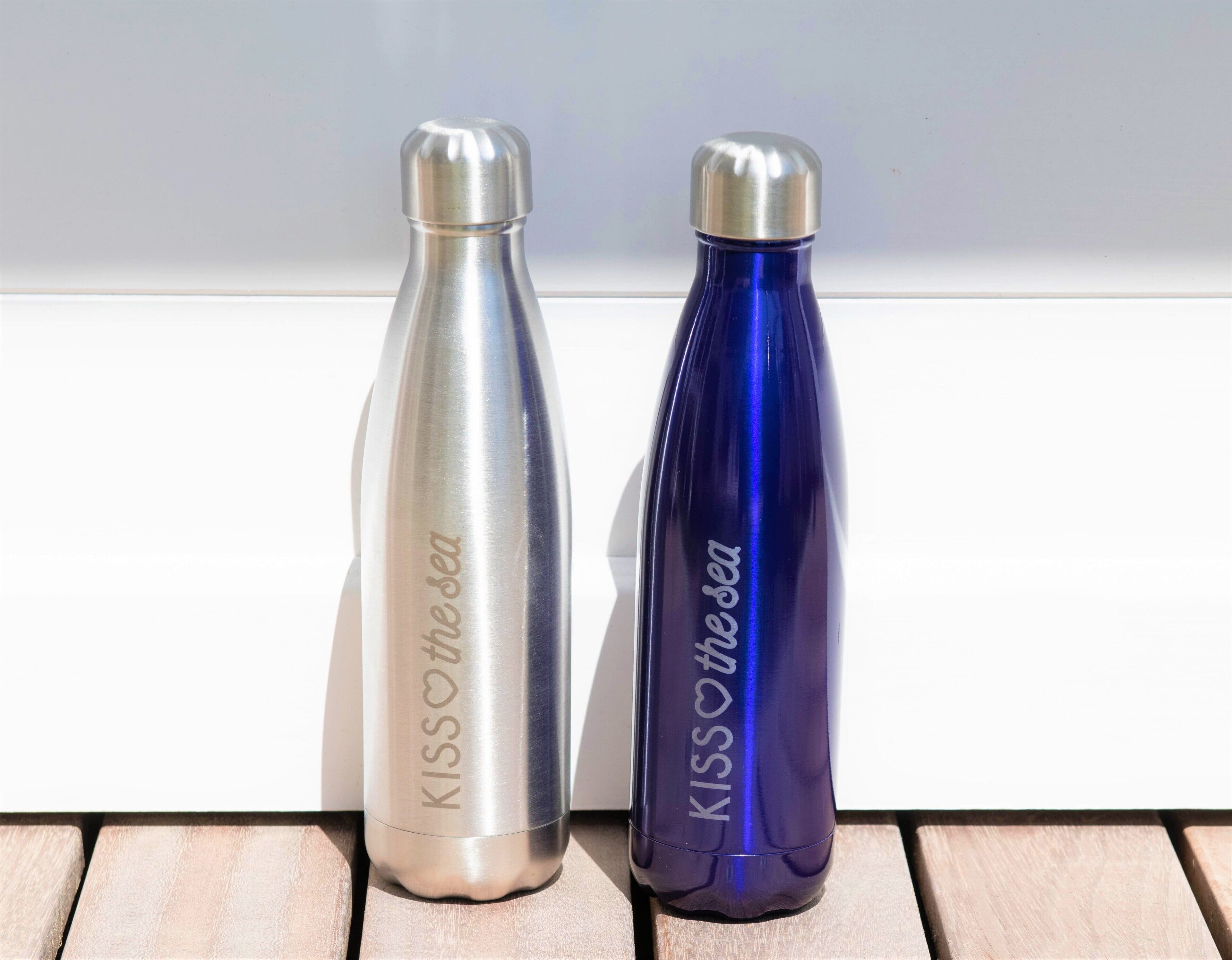 Two metallic water bottles with inscriptions, placed on a wooden surface against a white background.