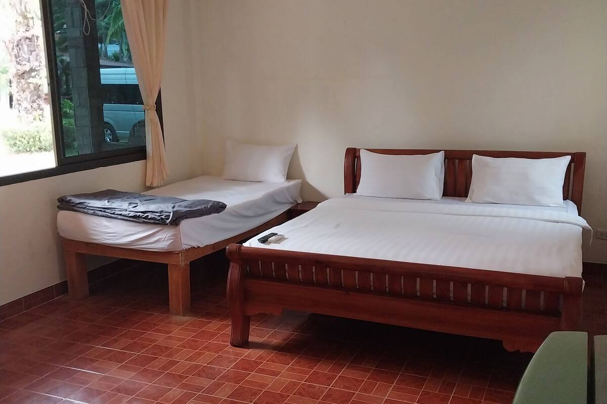 A room with two beds, a window with curtains, and a tiled floor.