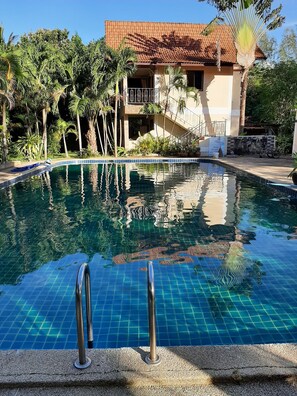 A swimming pool with clear blue water, surrounded by tropical plants and a building with a tiled roof. - Sofia Garden Resort (Ko Chang)