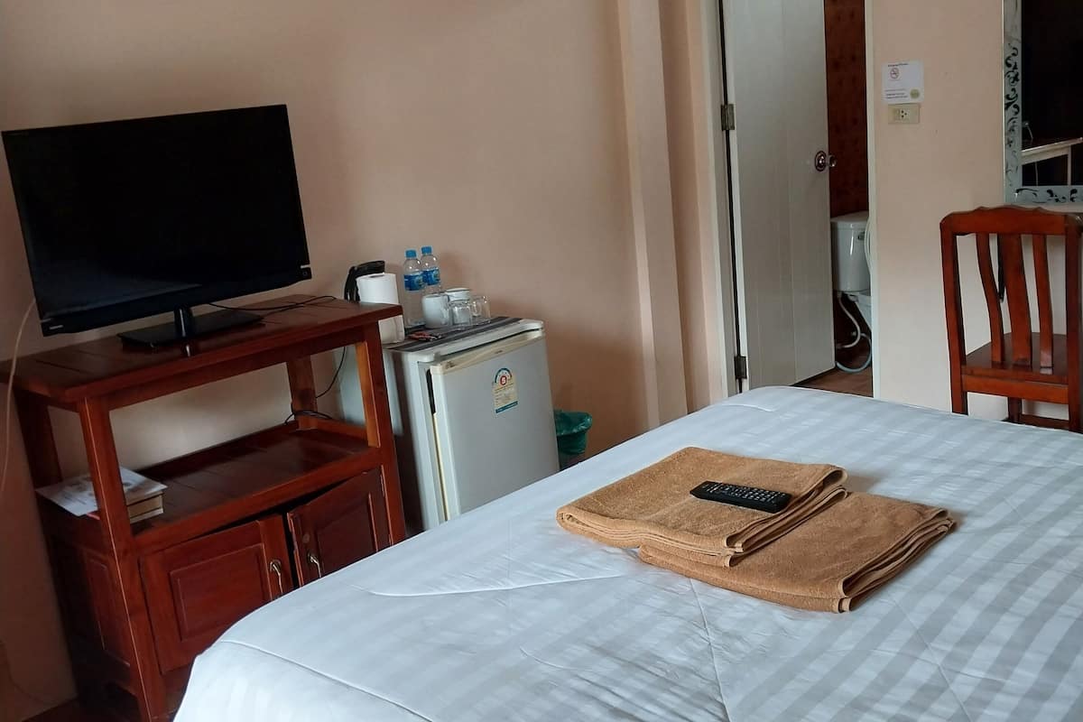 A hotel room with a bed, a TV on a wooden stand, a small fridge, and a door leading to a bathroom.