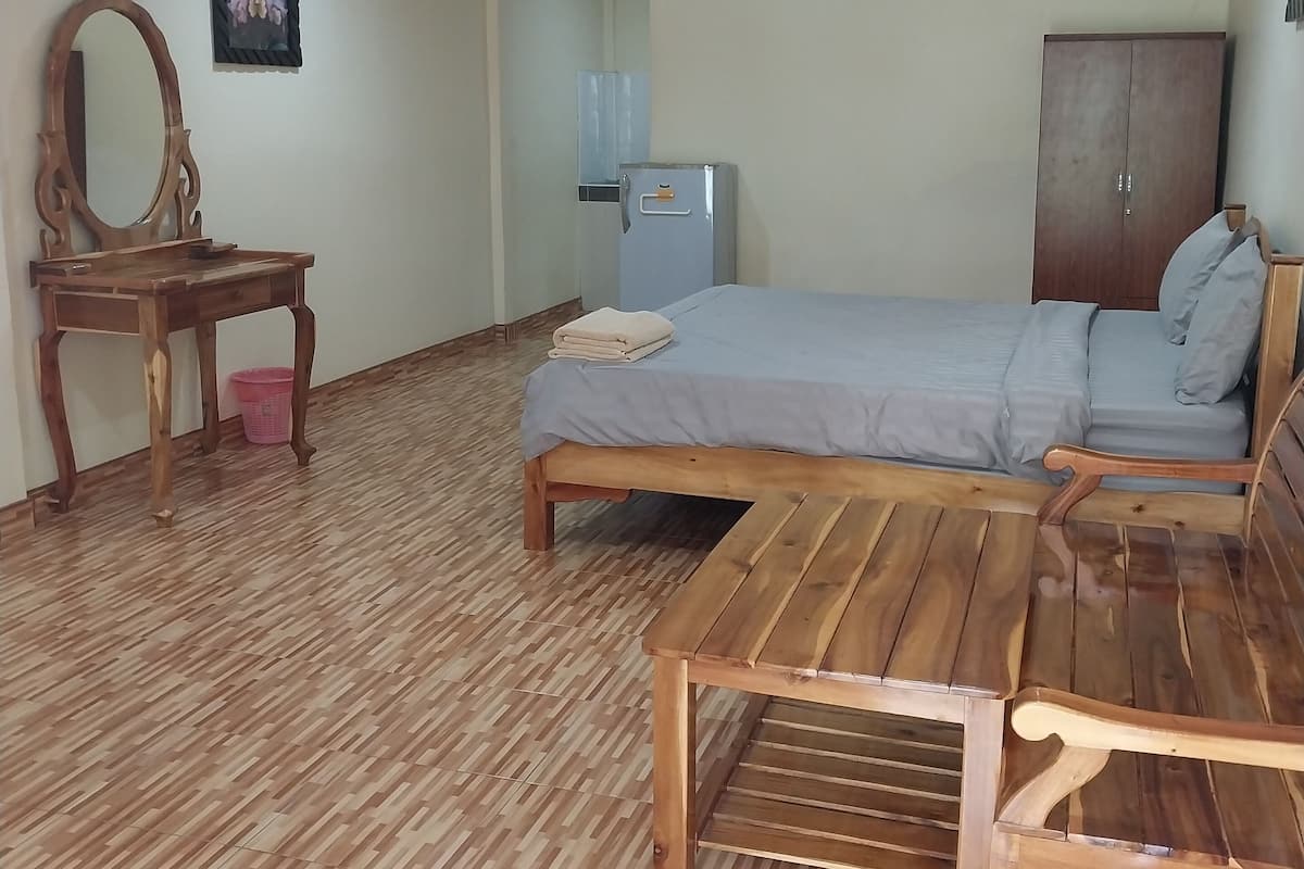 A room with a bed, wooden furniture, a desk, a mirror, and an air conditioning unit.