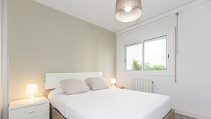 A bedroom with a bed, nightstands, a window, and a radiator. - UHC SOROLLA APARTMENTS (Salou)