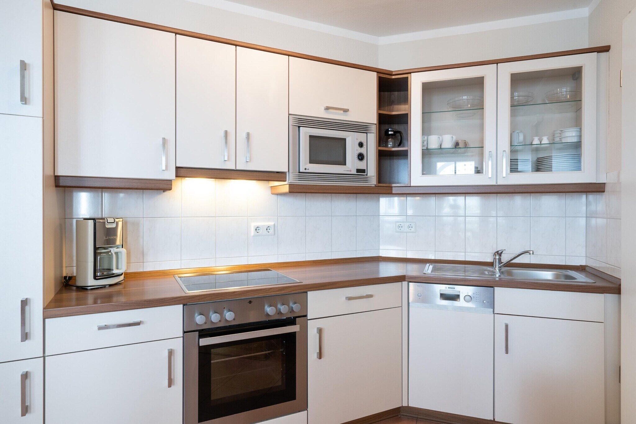 Een moderne keuken met witte kasten, een roestvrijstalen magnetron, een koffiezetapparaat, een vaatwasser en een houten aanrecht.