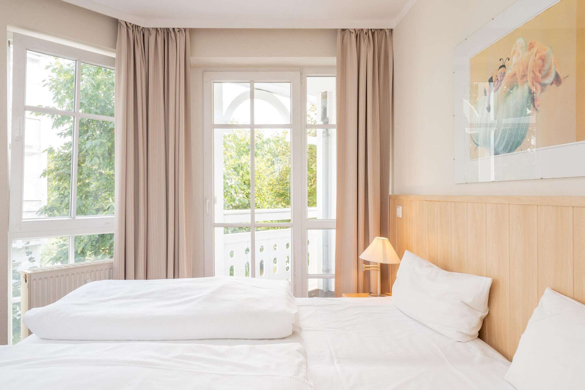 A hotel room with a large bed, a nightstand with a lamp, and a window with curtains.
