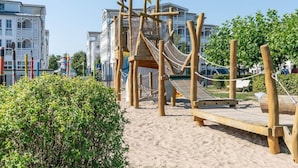 Un espace de jeux avec une structure d’escalade en bois et un toboggan, entouré de sable et de verdure.