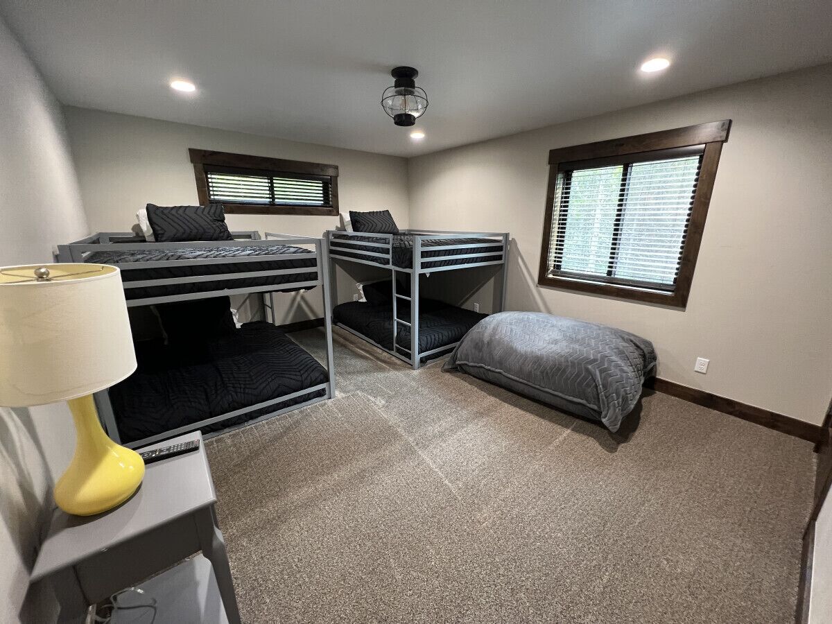 A compact room with bunk beds, a desk with a lamp, and a window with blinds.