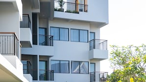 Un edificio residencial moderno de varios pisos con balcones, un césped cuidado y plantas en macetas.