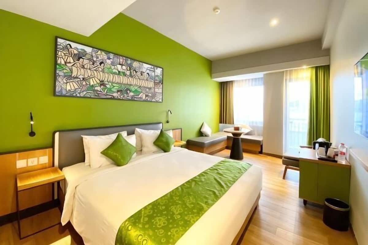 Quarto de hotel com uma cama grande, uma escrivaninha, uma cadeira, uma mesa pequena e uma janela com cortinas.